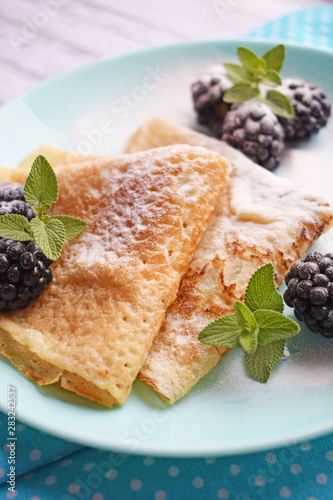Delicious hot pancakes with blackberries and mint on a wooden background. © NADEZHDA