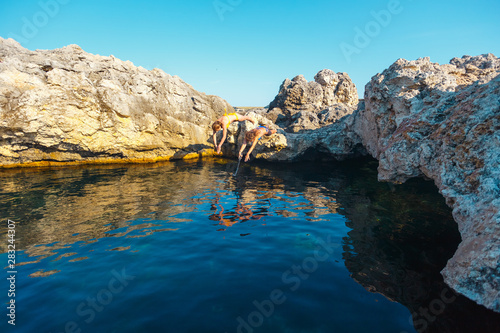 Two girls with a camera jump into the sea water from a cliff