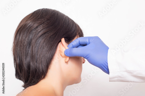 A plastic surgeon doctor examines a patient s girl s ears before performing an otoplasty surgery, close-up photo