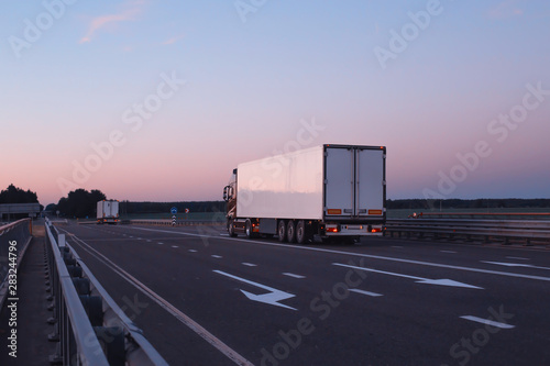 A convoy of trucks trucks transports the cargo in the evening on the highway, the concept of logistics and freight, copy space