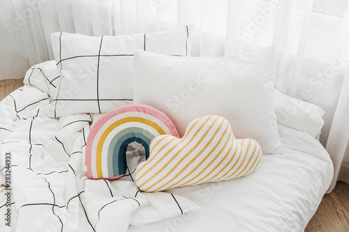 White bedding sheets with striped blanket and bright pillow. Messy bed.