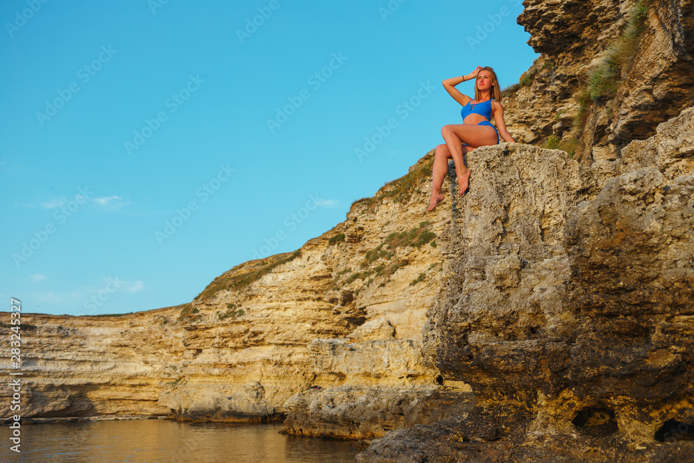 Girl in a blue swimsuit on a rocky seashore