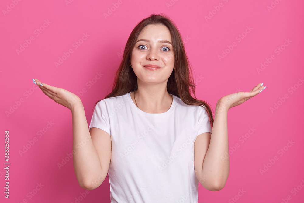 Portrait of smiling young woman wearing casual clothes, looking at camera, spreading hands aside isolated over pink background in studio. People lifestyle concept. Copy space for your advertisment. Portrait of smiling young woman wearing casual clothes, looking at camera, spreading hands aside isolated over pink background in studio. People lifestyle concept. Copy space for your advertisment.