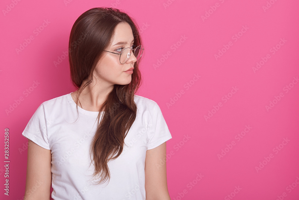 Portrait side profile of beautiful woman with long hair, dressed whitr casual t shirt and glasses, looking aside isolated ower pink studio background with copy space for your advertisment or promotion Portrait side profile of beautiful woman with long hair, dressed whitr casual t shirt and glasses, looking aside isolated ower pink studio background with copy space for your advertisment or promotion
