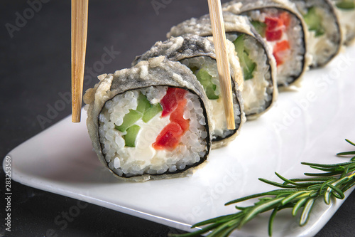 Sushi roll with chopsticks on a white plate close up. Gray background and rosemary