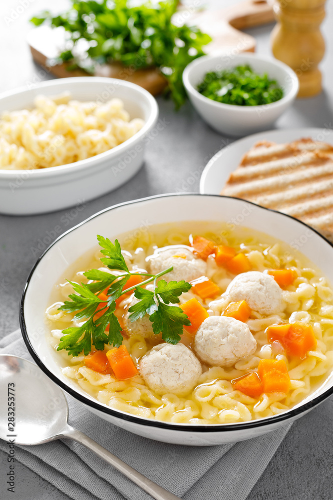 Hot chicken soup, broth with meatballs, carrot, pasta and fresh parsley