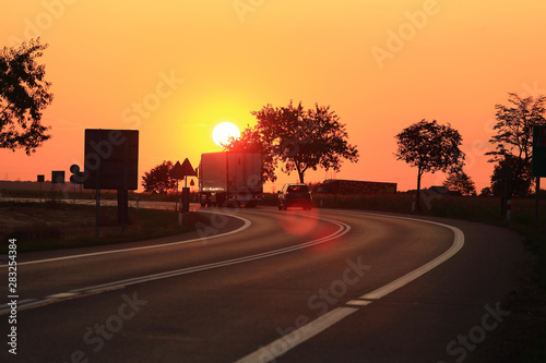 Samochód osobowy i ciężarowy, tir na tle zachodzącego słońca, droga ekspresowa. photo