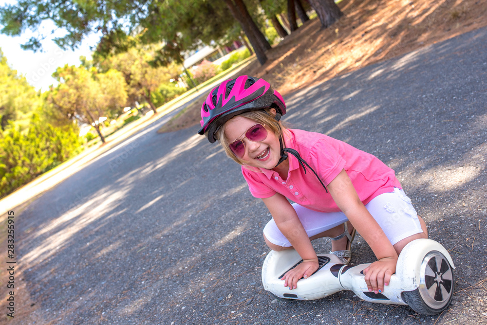 Adorable little smiling girl with hoverboard and safety helmet having fun outside in the park Adorable little smiling girl with hoverboard and safety helmet having fun outside in the park