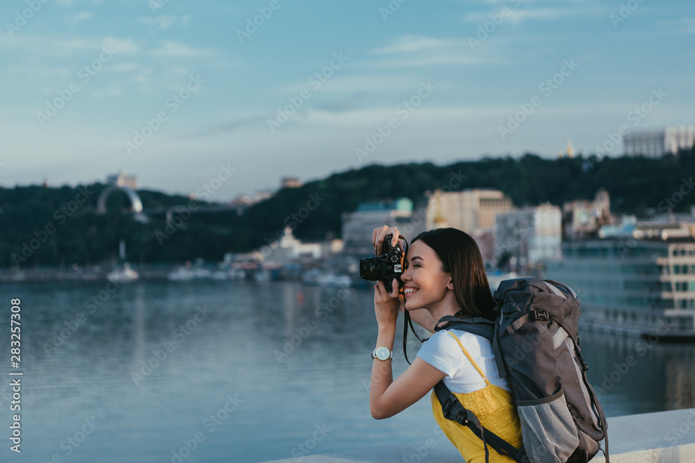 side view of asian woman with backpack taking photo