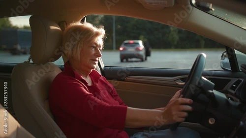 Portrait senior woman in new car look around sitting at the wheel happy adventure close up handheld drive customer free time holiday journey smiling summer travel vacation front view slow motion photo