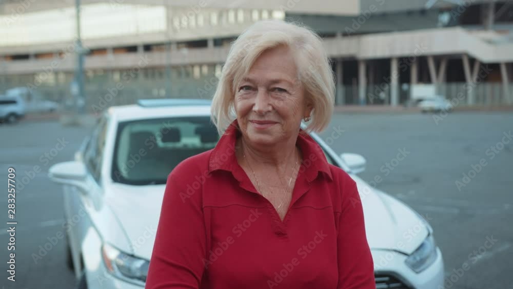 Smiling senior woman standing near car look at camera happy adventure close up handheld drive customer free time holiday journey vacation front view portrait slow motion Smiling senior woman standing near car look at camera happy adventure close up handheld drive customer free time holiday journey vacation front view portrait slow motion