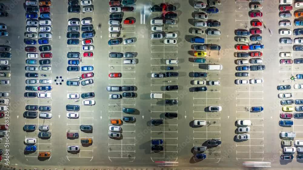 Aerial top view of the supermarket (hypermarket or shopping mall) parking lot with lots of cars at night. Time lapse