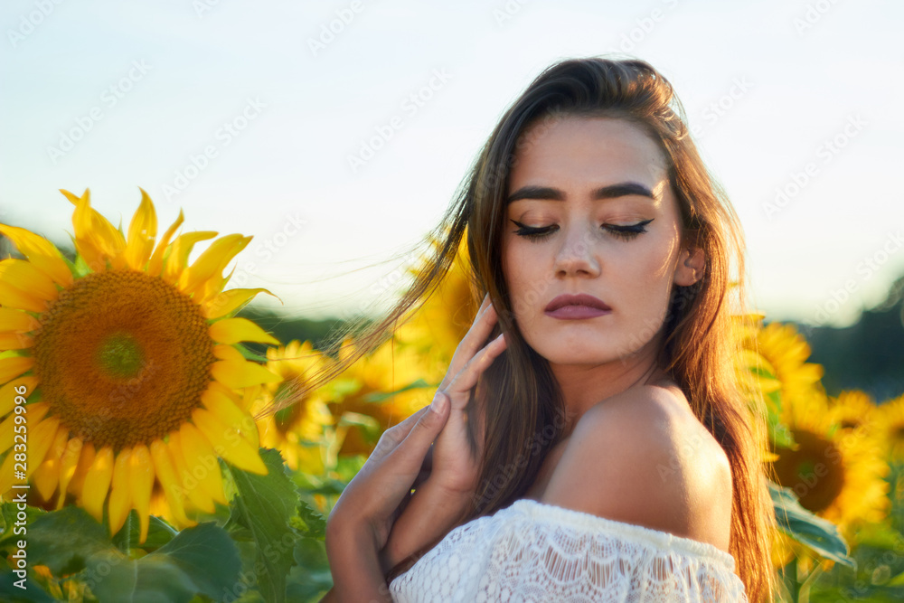 Beautiful young girl enjoying nature on a field of sunflowers. Sunlight plays on the field. Outdoor lifestyle. Summer cozy mood. Beautiful young girl enjoying nature on a field of sunflowers. Sunlight plays on the field. Outdoor lifestyle. Summer cozy mood.