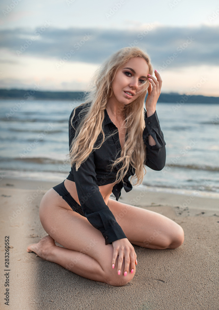 Slim sexy blonde girl kneeling on the beach at sunset. Touching her hair. Slim sexy blonde girl kneeling on the beach at sunset. Touching her hair.