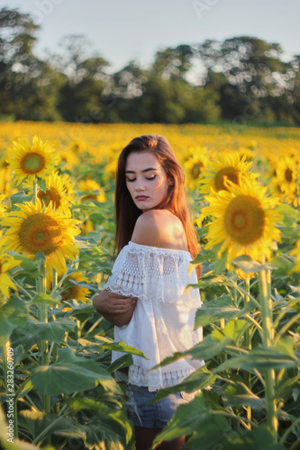 Beautiful young girl enjoying nature on a field of sunflowers. Sunlight plays on the field. Outdoor lifestyle. Summer cozy mood.