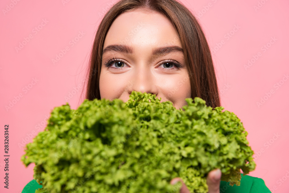 front view of attractive young woman holding lettuce and looking at camera isolated on pink front view of attractive young woman holding lettuce and looking at camera isolated on pink