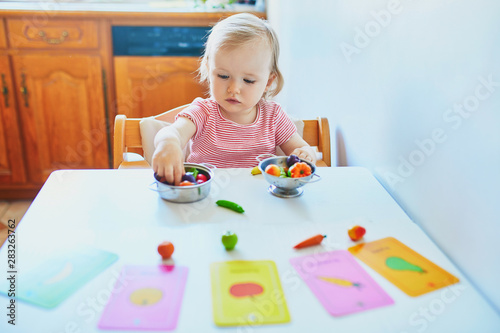 Adorable little girl playing with toy fruits and vegetables