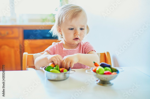 Adorable little girl playing with toy fruits and vegetables