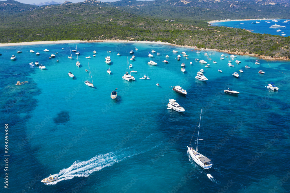 View from above, stunning aerial view of a beautiful bay full of boats and luxury yachts. A turquoise sea bathes the green and rocky coasts. Liscia Ruja, Emerald Coast (Costa Smeralda) Sardinia, Italy