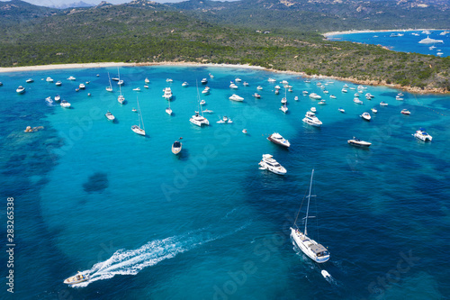 Obraz na płótnie View from above, stunning aerial view of a beautiful bay full of boats and luxury yachts. A turquoise sea bathes the green and rocky coasts. Liscia Ruja, Emerald Coast Sardinia, Italy w salonie