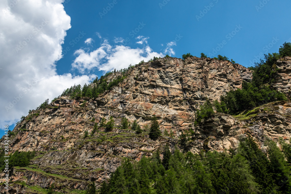 Sheer cliff with trees on a beautiful sunny day with blue sky and clouds