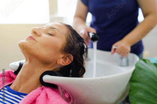 Hairdresser washing hair of woman female customer with a shower at the saloon applying shampoo on wet hair
