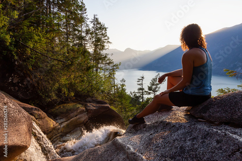 Adventurous Girl is sitting on top of a Beautiful Waterfall  Shannon Falls  and watching the sunset. Taken near Squamish  North of Vancouver  British Columbia  Canada.