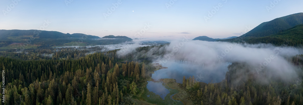 Aerial Panoramic View of Fairy Lake covered in clouds during a vibrant summer sunrise. Taken near Port Renfrew, Vancouver Island, British Columbia, Canada. Aerial Panoramic View of Fairy Lake covered in clouds during a vibrant summer sunrise. Taken near Port Renfrew, Vancouver Island, British Columbia, Canada.