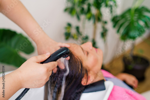 Hairdresser washing hair of woman female customer with a shower at the saloon