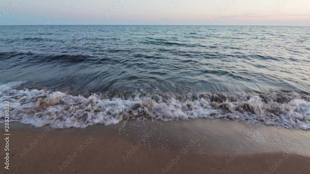 Waves lapping on a sandy kefalonia beach at sunset, with a warm glow on the horizon Waves lapping on a sandy kefalonia beach at sunset, with a warm glow on the horizon