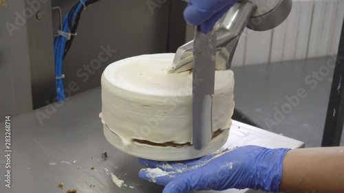 Pastry chef puts cream on biscuit sponge cake using equipment. Manual manufacture of sweets desserts. Confectioner covers the torte with a layer of cream. Flour confectionery production. photo