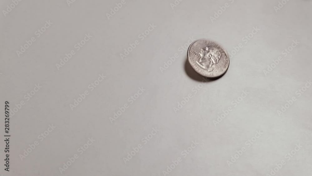 A quarter-dollar coin and another one-cent coin rotate and stop in the frame. Copy space. US small metal money moving on a white table. A quarter-dollar coin and another one-cent coin rotate and stop in the frame. Copy space. US small metal money moving on a white table.