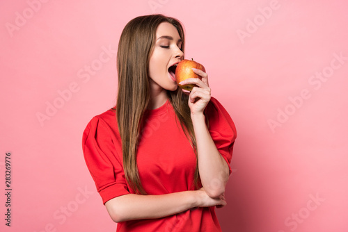 attractive young woman eating apple with closed eyes on pink