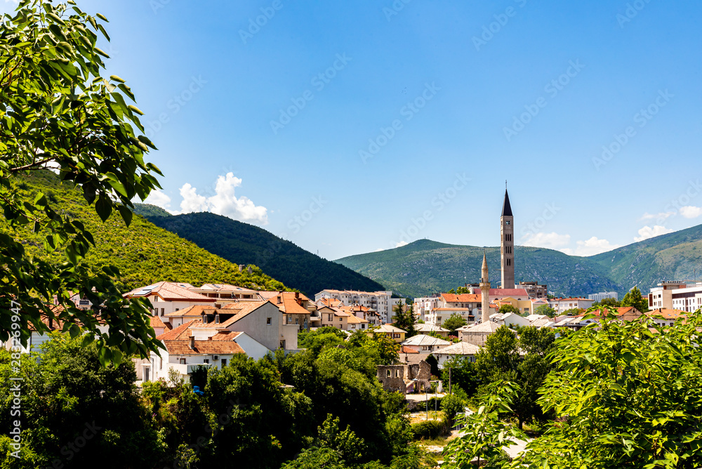 A bell tower and a minaret in Mostar with mountains