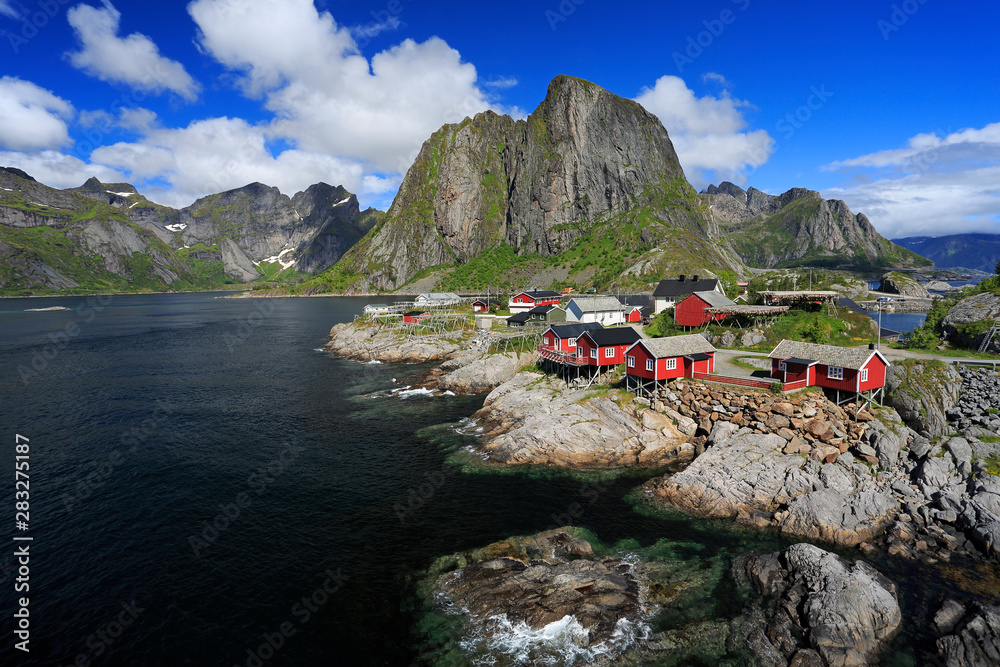 Traditional red colorful Norwegian fishing houses in Reine with mountains on the background, Lofoten Islands in northern Norway