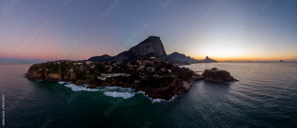 Panoramic view of the coastline and beach of Joatinga in Rio de Janeiro with its beautiful picturesque natural richness and far in the background the well known landmark peaks of the city at daybreak