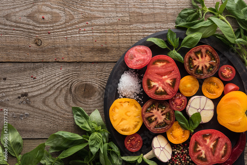 top view of tomatoes, garlic, chilli pepper, salt and pepper on pizza pan near spinach on wooden table