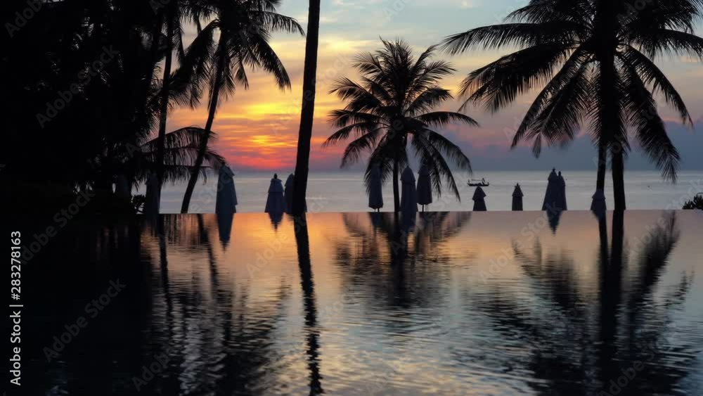 Sun setting over pool with ocean and palm tree silhouettes background Sun setting over pool with ocean and palm tree silhouettes background