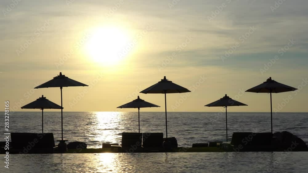 The sun rises at the beach with umbrellas in the foreground The sun rises at the beach with umbrellas in the foreground