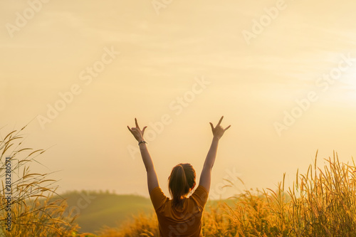 Asian woman standing in meadow and show hand up with love sign at sunrise time, Selective focus, Copy space.