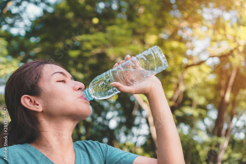Young asian woman runner relaxing drinking water in bottle in the park outdoors after sport at early morning time, Exercise and healthy concept,