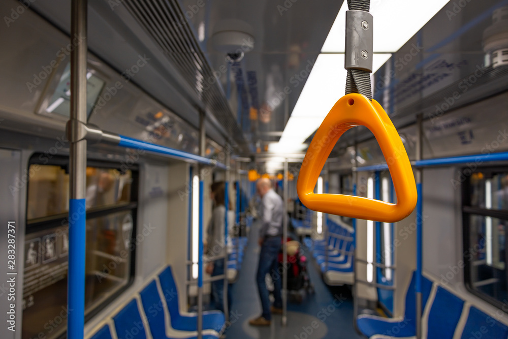 A yellow hand grip over background of an almost empty subway train, passengers with a baby stroller ready to drop off.