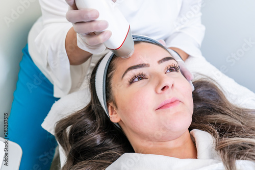 Beauty treatment using microneedling device with radio frequency to tighten skin. Used on the forehead of a woman during treatment.