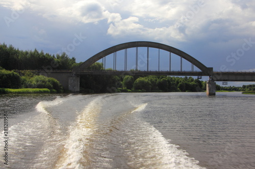 Russian landscape, arched railway bridge over the river Nerl in Sknyatino Tver region on summer day against the blue sky, the view from stern of the motor boat photo