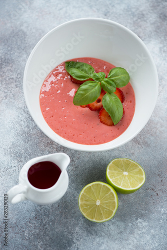 Bowl of cold soup with fresh strawberries, vertical shot on a beige stone background
