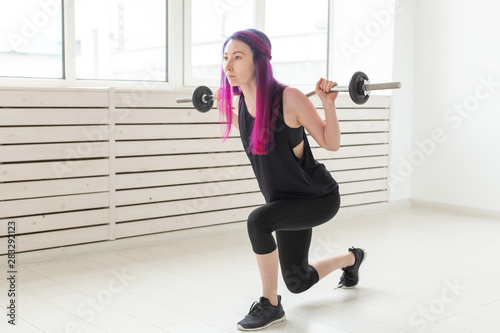 Fitness, sport, people concept - young woman in sport suit is squatting with bar