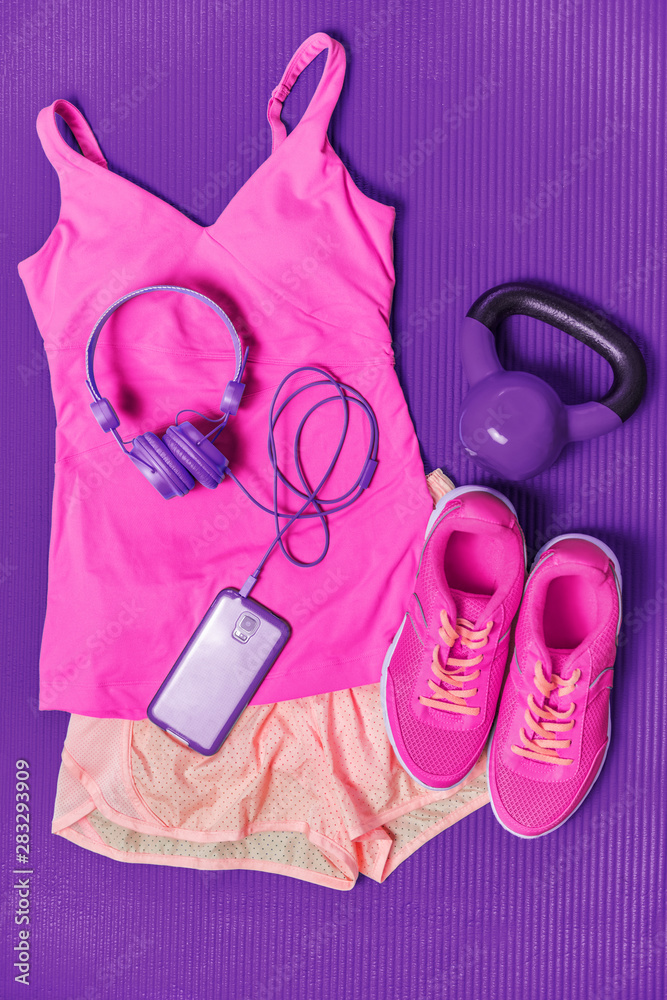 Activewear fitness clothes outfit - cute pink fashion matching clothing for  girl training with weights and phone headphones to listen to music during  workout at gym on purple exercise mat background. Photos