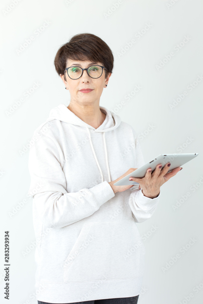 Cute middle-aged woman in casual clothes is looking online stores using a tablet on a white background. Concept of wireless internet and online shopping. Copyspace.
