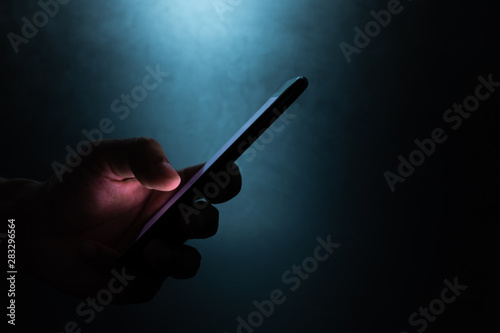 Fototapeta Naklejka Na Ścianę i Meble -  silhouette hand holding and touching a mobile phone screen in the dark darkness against dark blue background