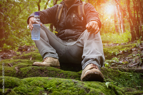 Hiking with a backpack and climbing shoes on a man sit on a moss covered forest and Hand holding a water bottle.